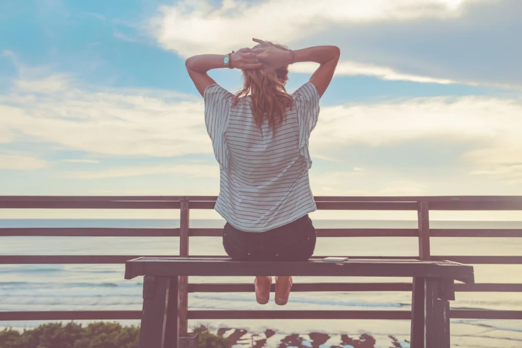 A happy person stretching on a bench at the beach. 