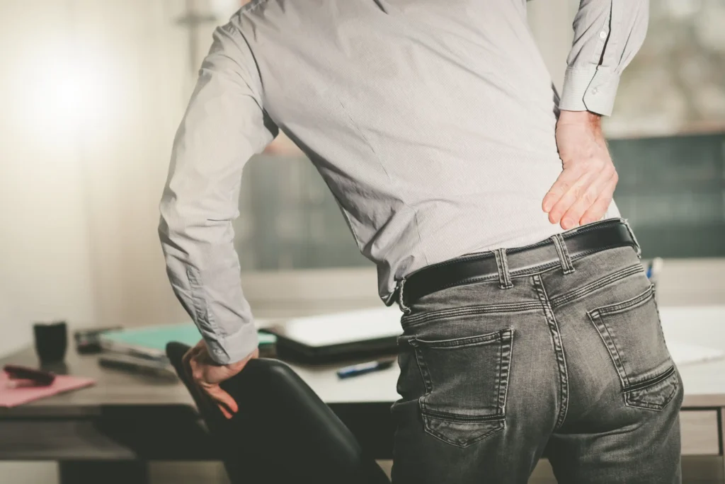 A man with his hand on a chair and holding his back because of chronic pain.