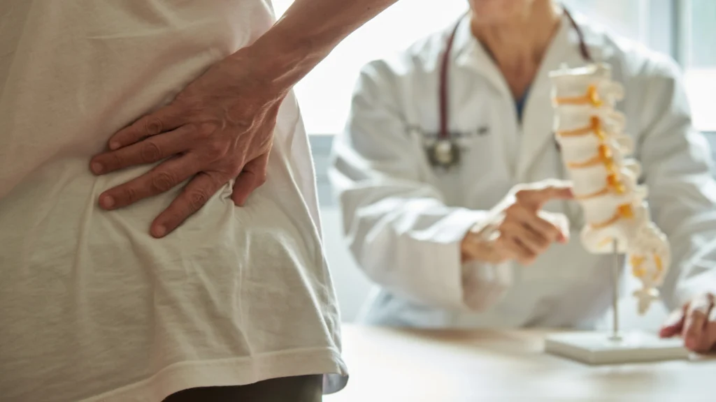 Patient holding lower back while doctor explains spine model during consultation.