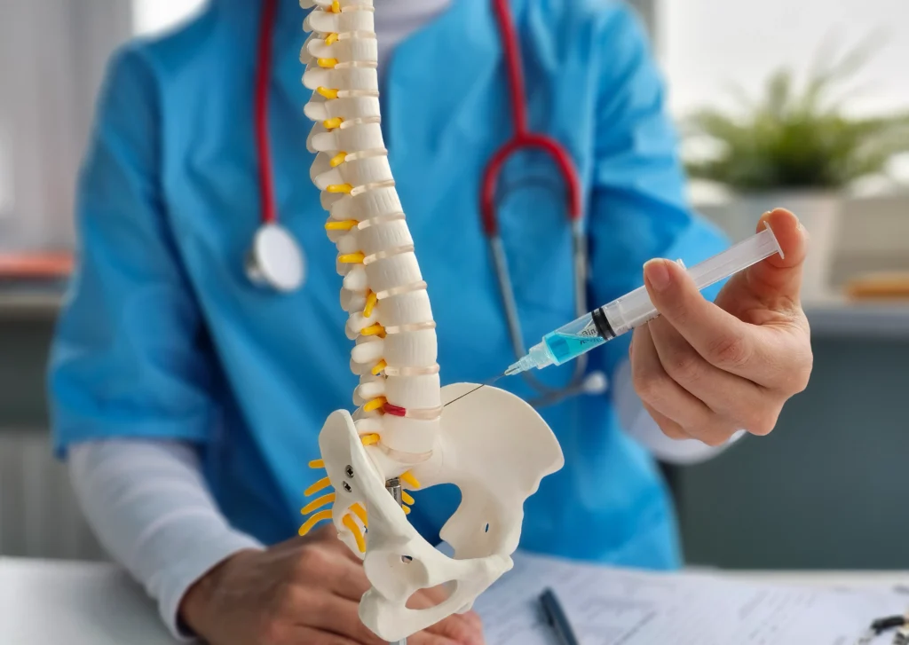 A doctor demonstrating treatment options for severe lower back pain using a spine model and an injection to show a procedure.