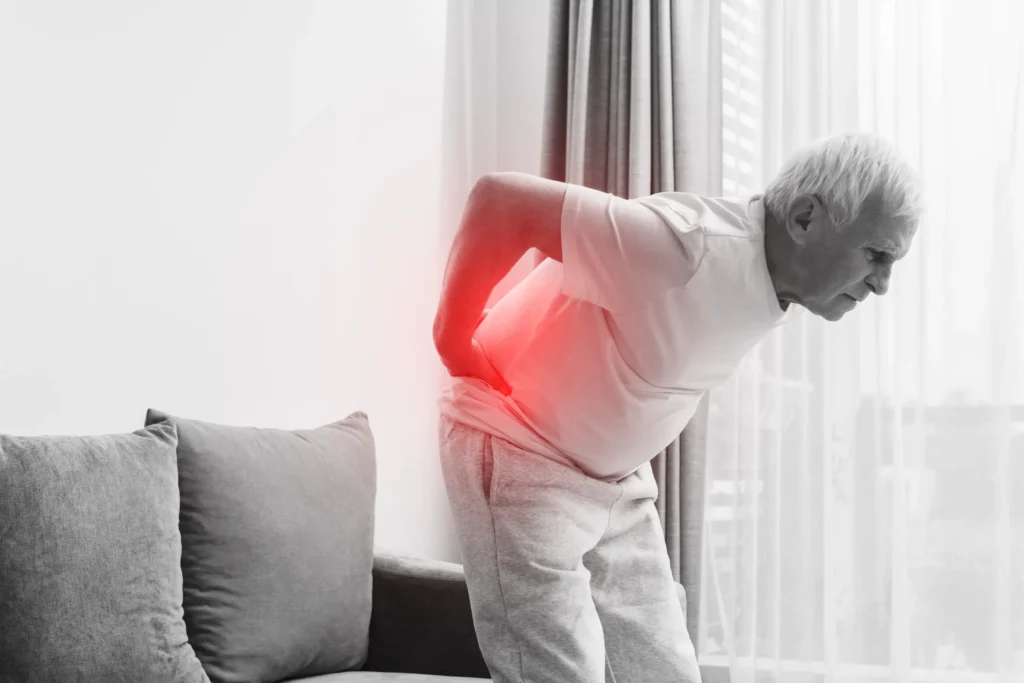 Older man leaning forward and holding his lower back in pain, with red highlighting to indicate the source of discomfort, representing chronic pain treated by spinal cord stimulation.