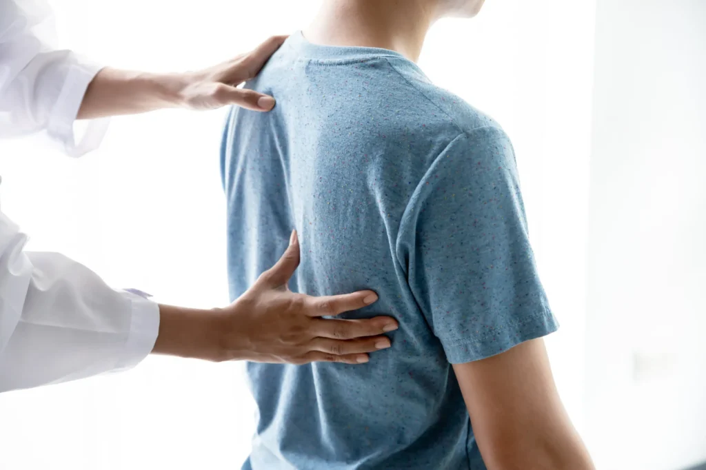 Medical professional examining a patient's upper back, possibly evaluating spinal alignment or preparing for a kyphoplasty procedure to treat a compression fracture.